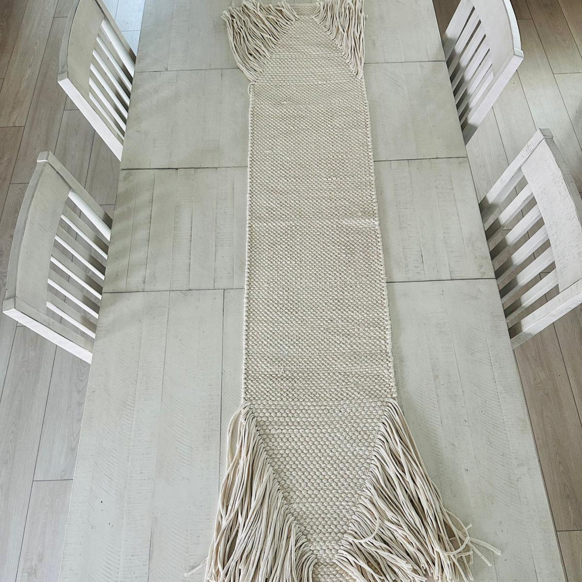 Beige woven table runner with tassels on a wooden dining table.