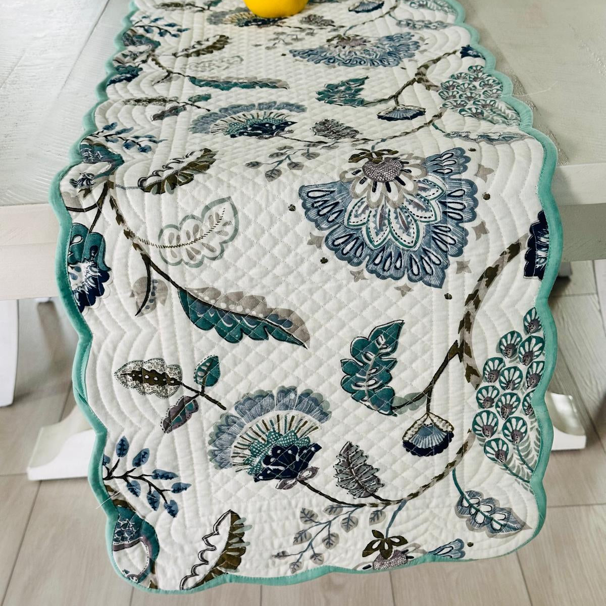 Floral patterned table runner on a wooden table with a yellow vase.