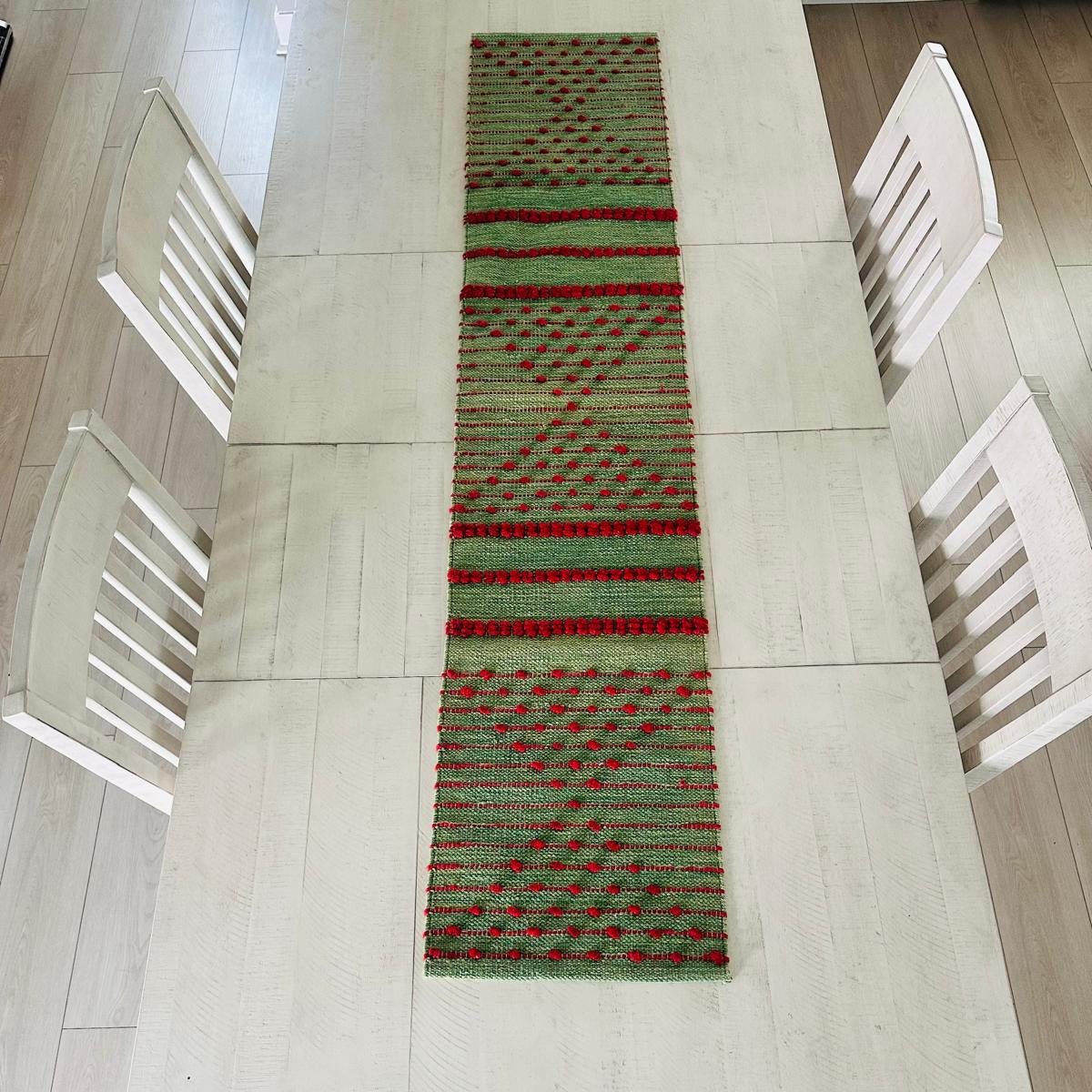 Green and red patterned table runner on a white table with white chairs.