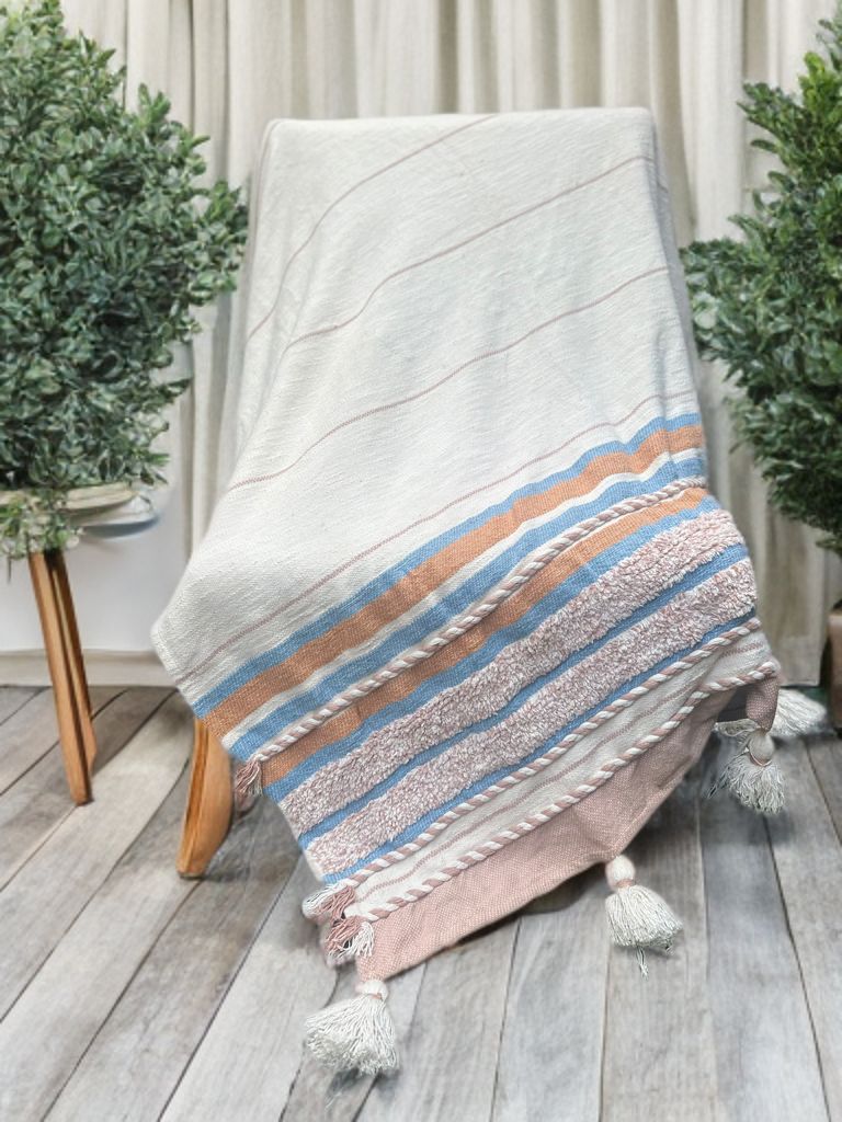 Textile with striped pattern draped over a chair on a wooden floor with plants in the background