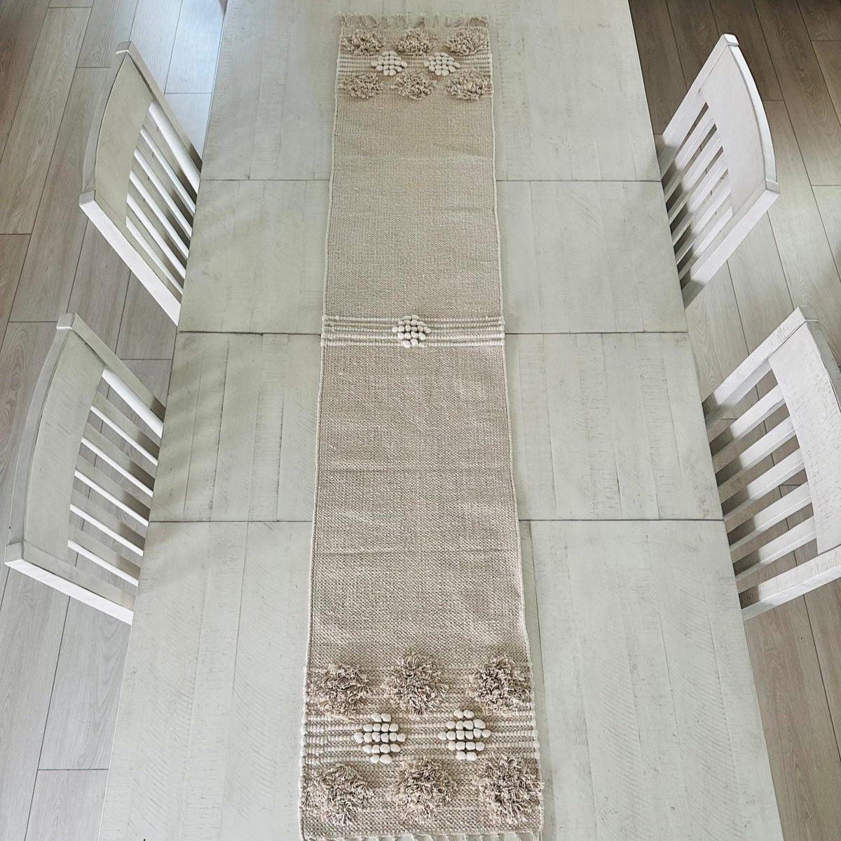 Decorative table runner on a dining table with white chairs.