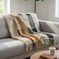 Plaid blanket draped over a sofa in a living room with a plant and coffee cup in the background.