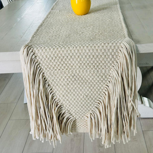 Beige woven table runner with fringe on a wooden table