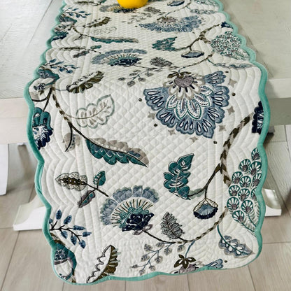 Floral patterned table runner on a wooden table with a yellow vase.