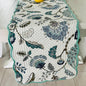 Floral patterned table runner on a wooden table with a yellow vase.