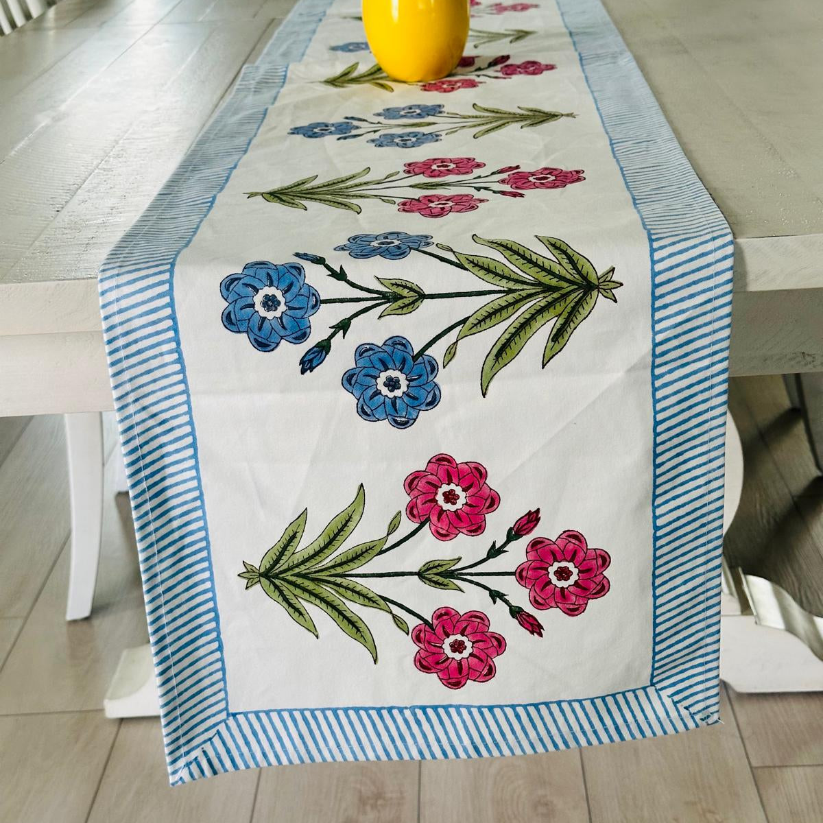 Embroidered floral table runner on a dining table with a yellow vase.