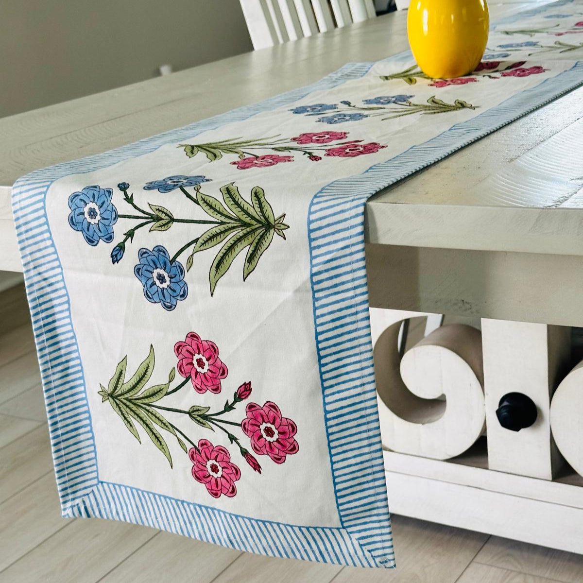 Floral embroidered table runner on a wooden table with a decorative cabinet in the background.