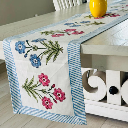 Floral embroidered table runner on a wooden table with a decorative cabinet in the background.