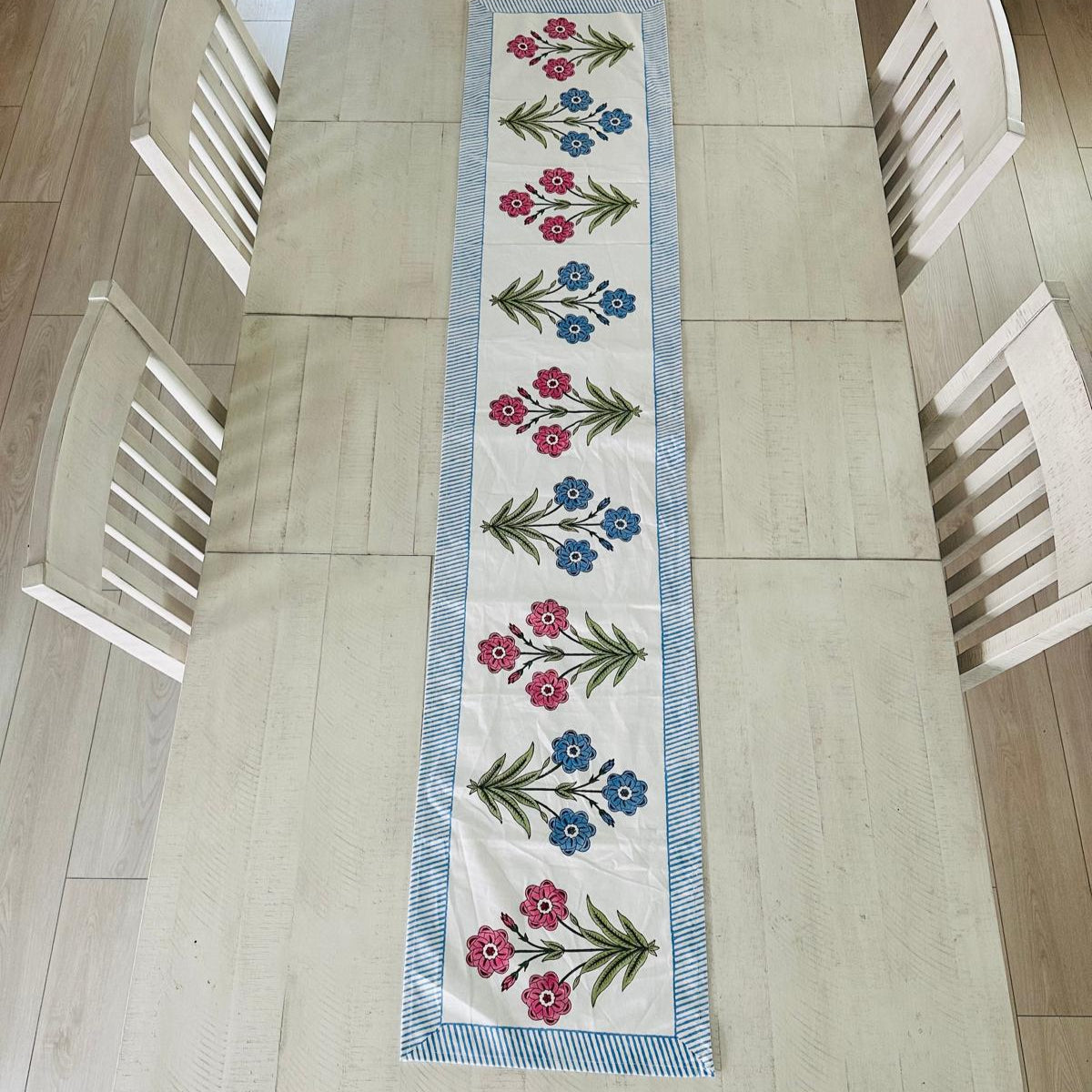 Floral table runner on a wooden table with chairs around it
