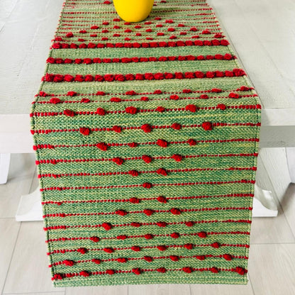 Green and red woven table runner on a white surface with a yellow vase.