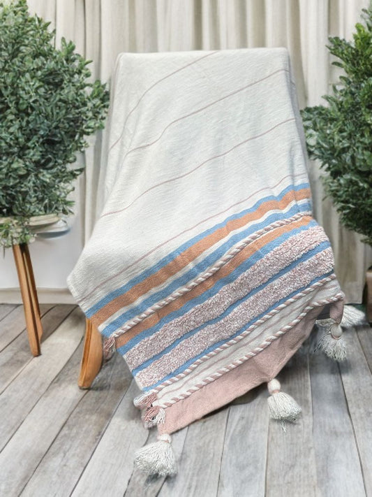 Textile with striped pattern draped over a chair on a wooden floor with plants in the background