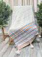 Textile with striped pattern draped over a chair on a wooden floor with plants in the background