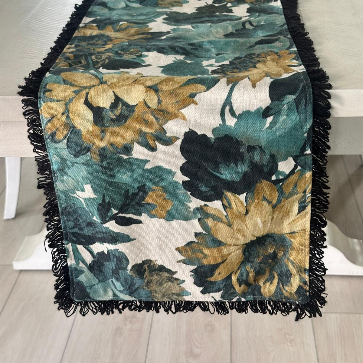 Floral patterned table runner with black fringe on a wooden table.