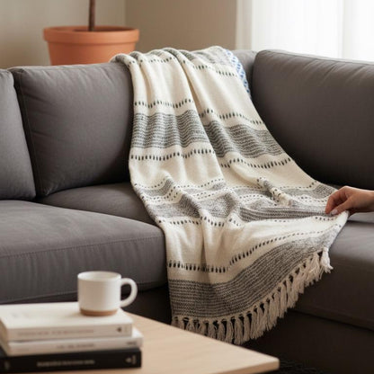 Gray sofa with a white and gray patterned throw blanket, coffee cup, books, and slippers on a wooden coffee table.