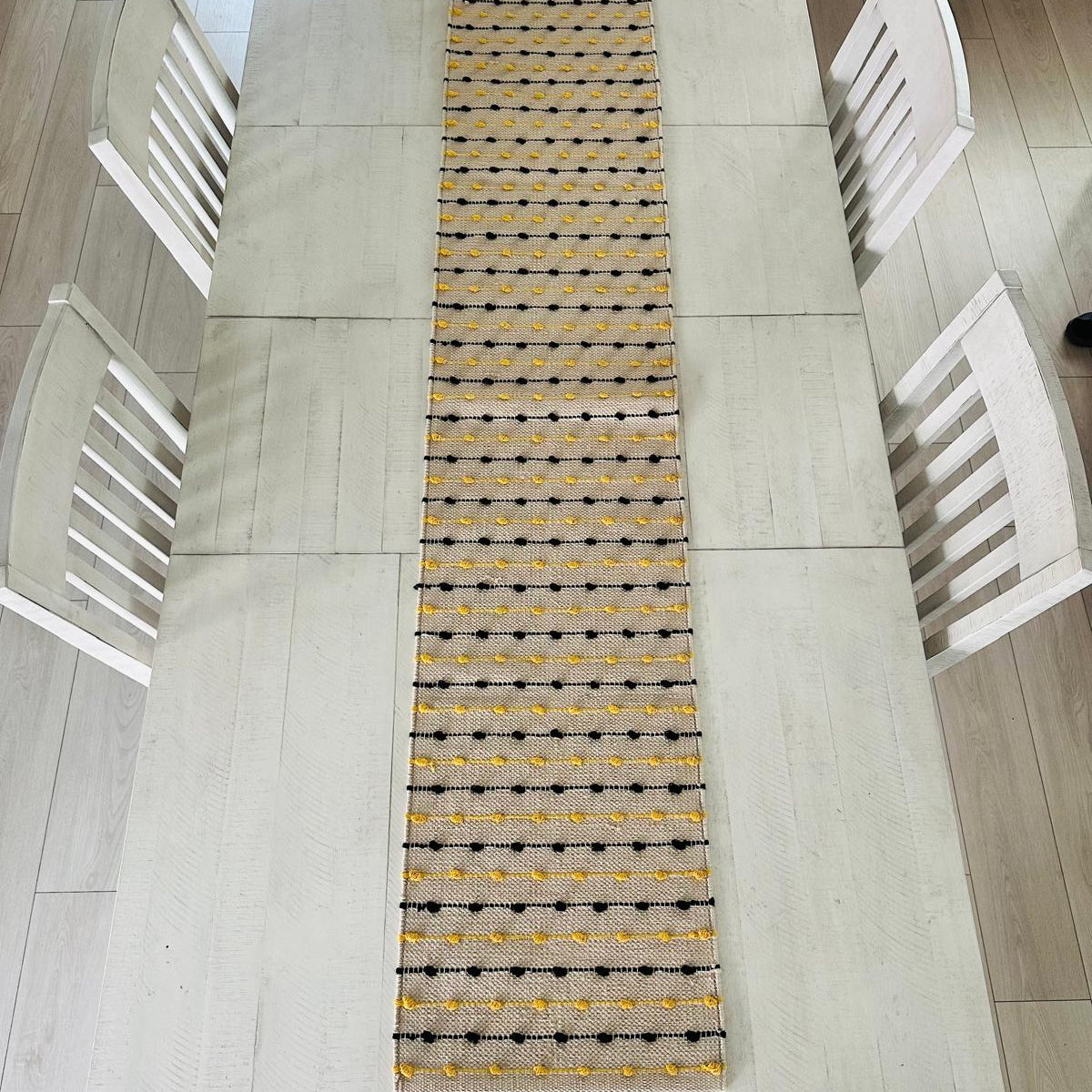 Dining table with a yellow and black patterned runner and white chairs.
