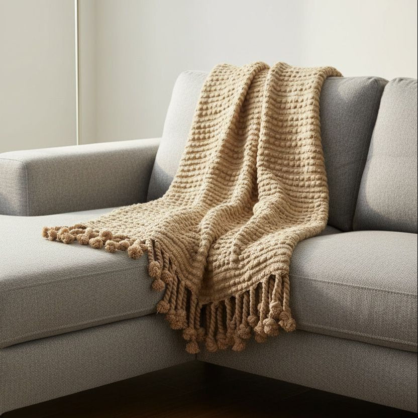 Gray sectional sofa with a beige knitted blanket in a living room setting.