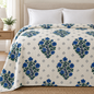 Bed-styled mockup of an ivory quilt with cobalt-blue floral bouquets, green foliage and gray diamond motifs.