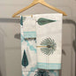 Folded fabric with palm tree pattern on a wooden hanger against a neutral background
