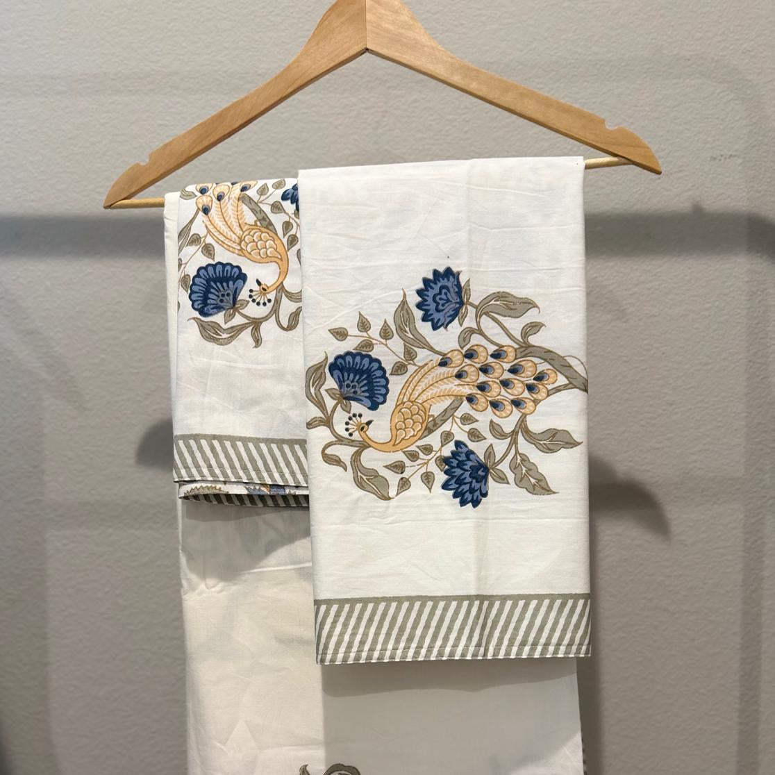 Embroidered fabric with peacock designs on a hanger against a gray background