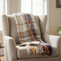 Beige armchair with a plaid blanket, open book, and coffee cup in a cozy living room.