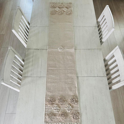 Decorative table runner on a dining table with white chairs.